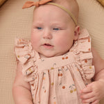 Close-up of a baby wearing the blush pink Rylee & Cru Ruffle Romper in Cherries