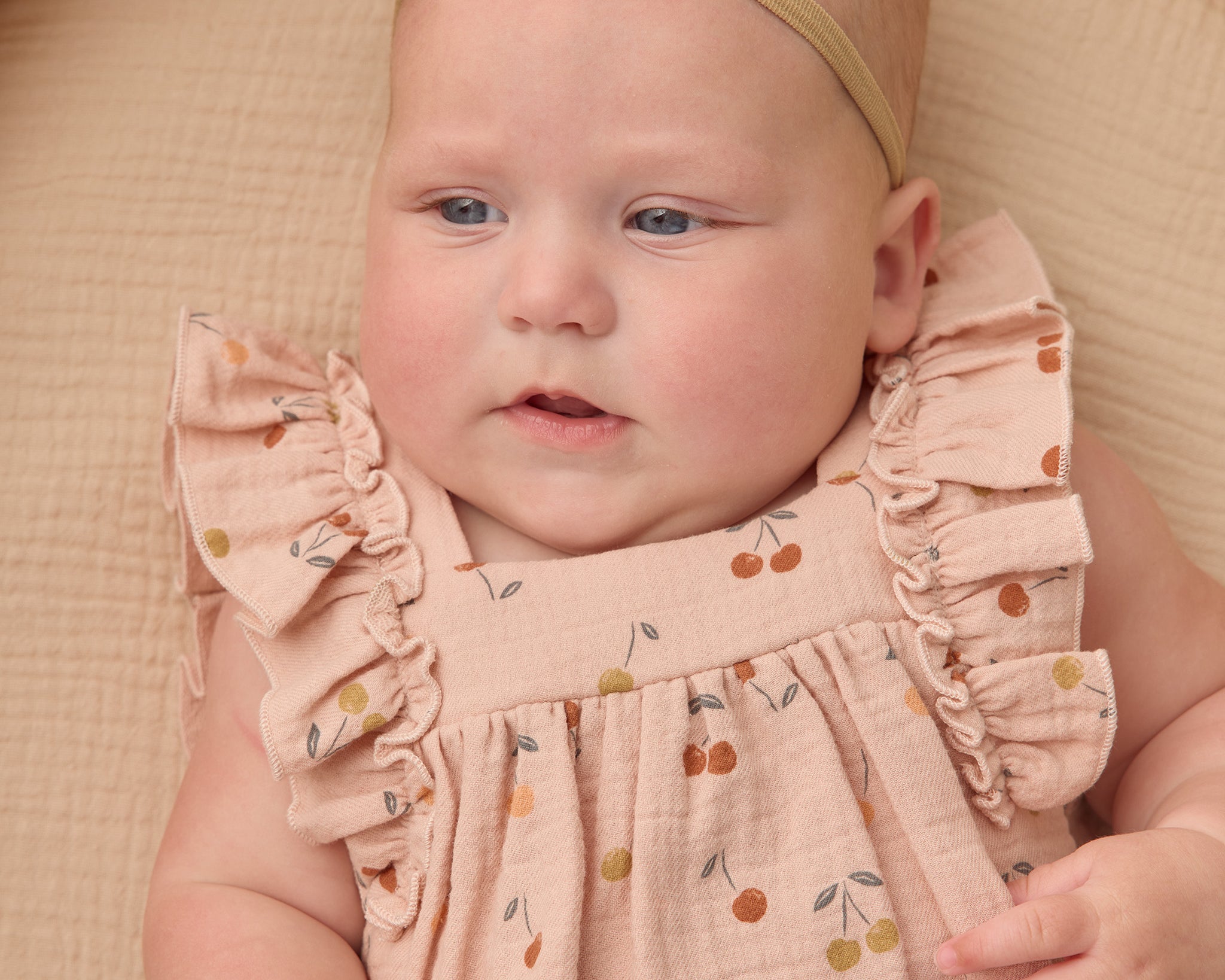 Close-up of a baby wearing the blush pink Rylee & Cru Ruffle Romper in Cherries