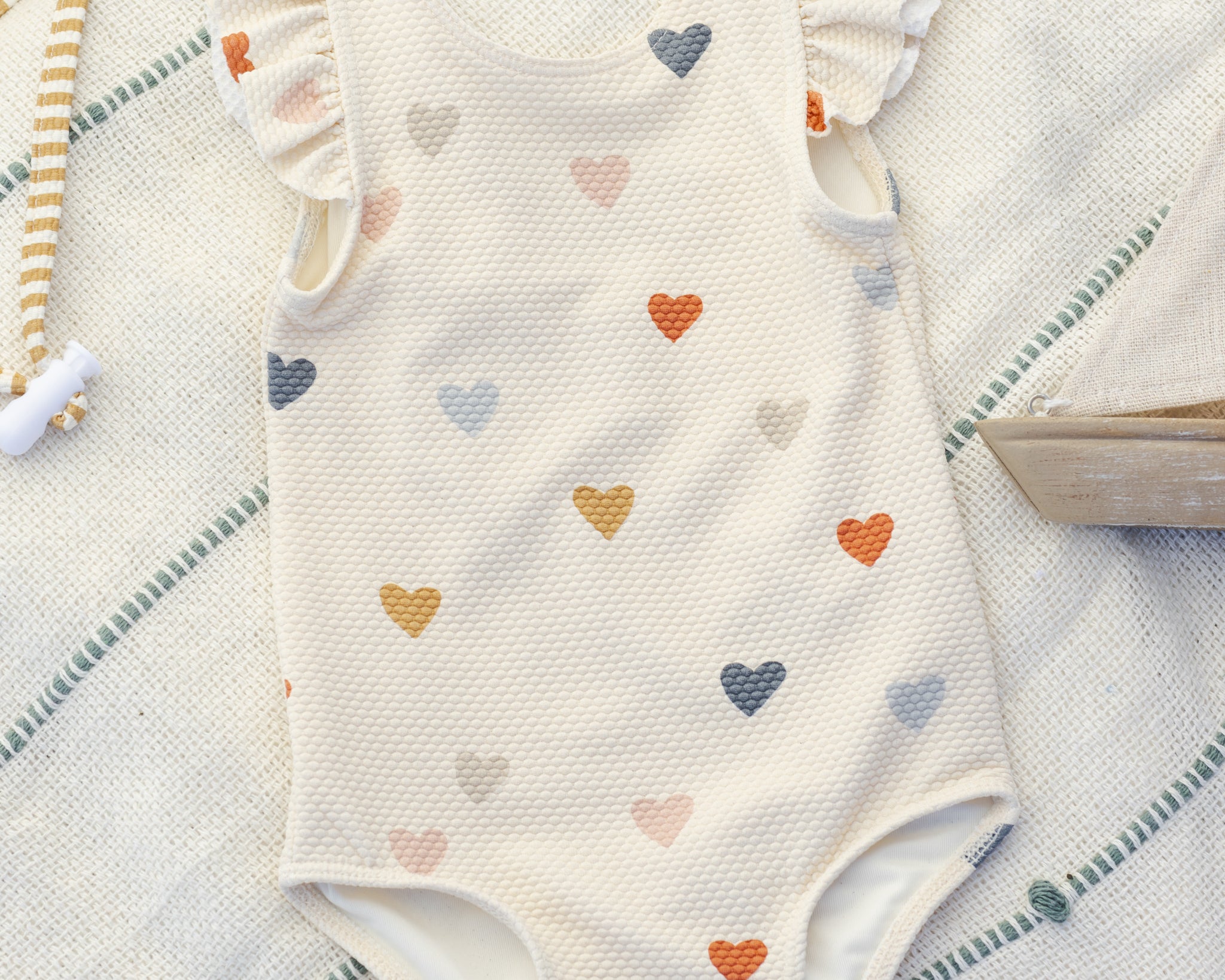 Rylee & Cru Scoop Back One-Piece Swimsuit in Confetti Hearts on a striped towel, angled view