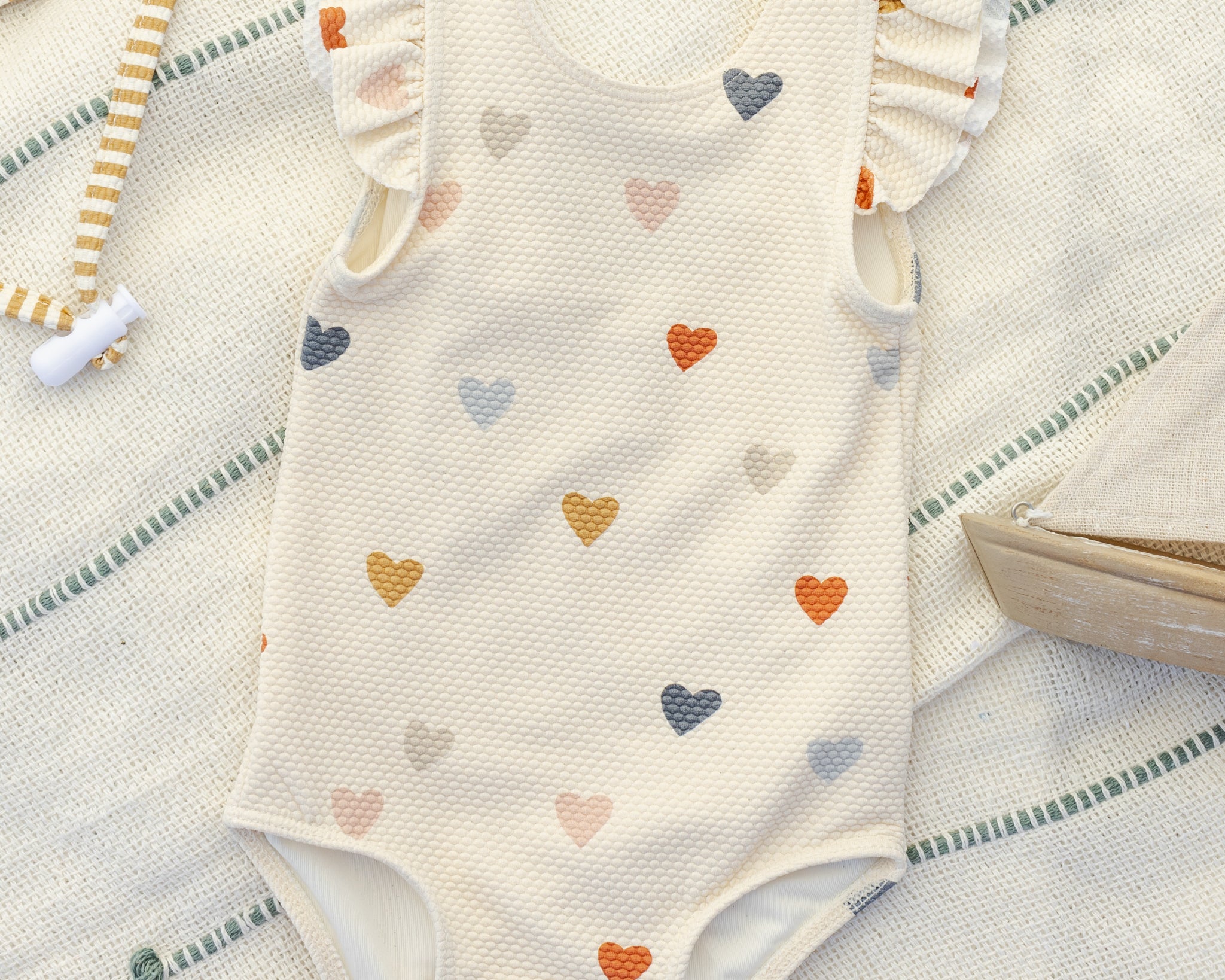 Rylee & Cru Scoop Back One-Piece Swimsuit in Confetti Hearts laid on a striped towel