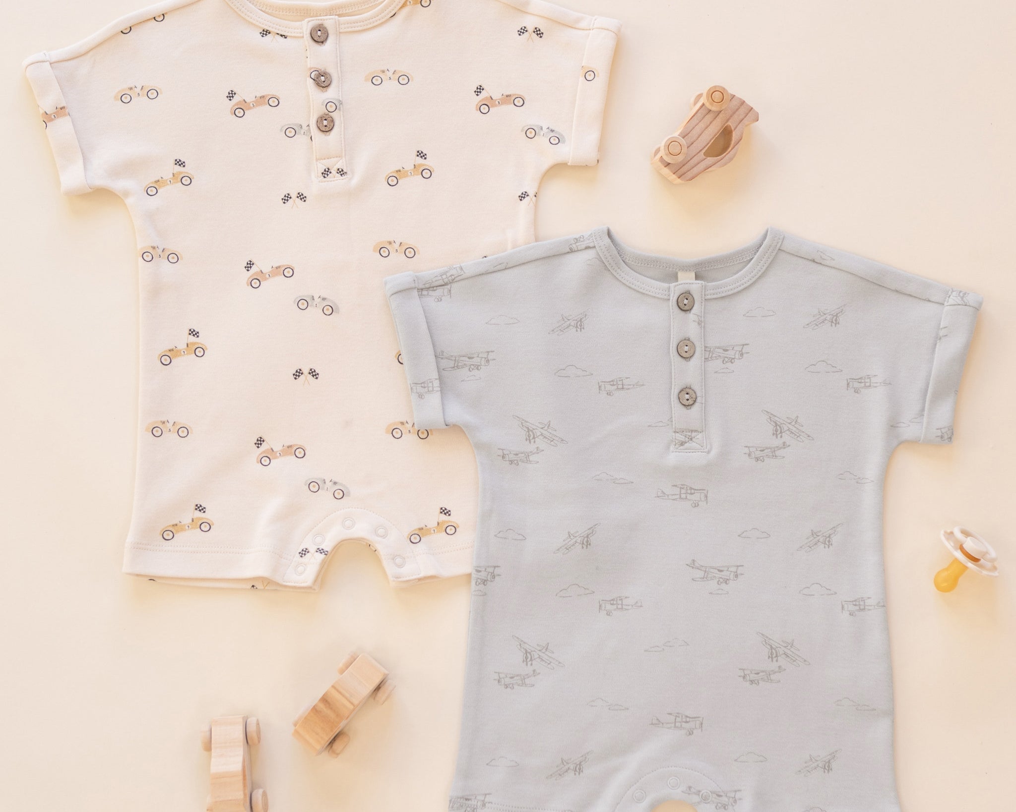Rylee & Cru Short Sleeve One-Pieces in Race Car and Airplanes laid out with wooden toys