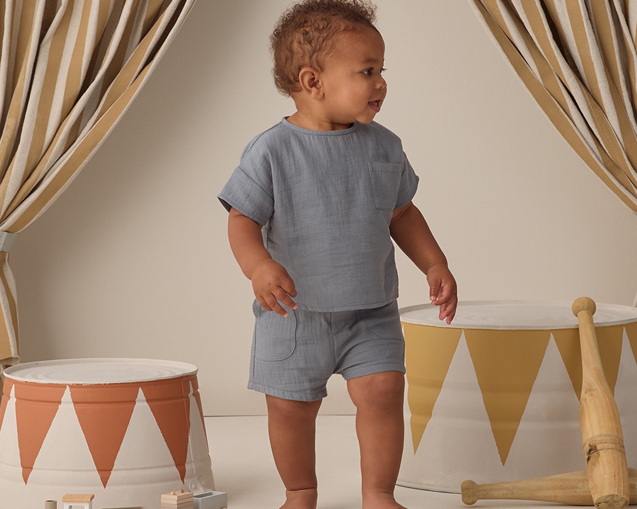 Toddler in a blue gauze set walking past striped drums wearing the Rylee & Cru Utility Short in Ocean