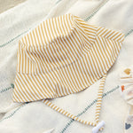 Rylee & Cru Youth Bucket Hat in Honey Stripe laid on a striped blanket
