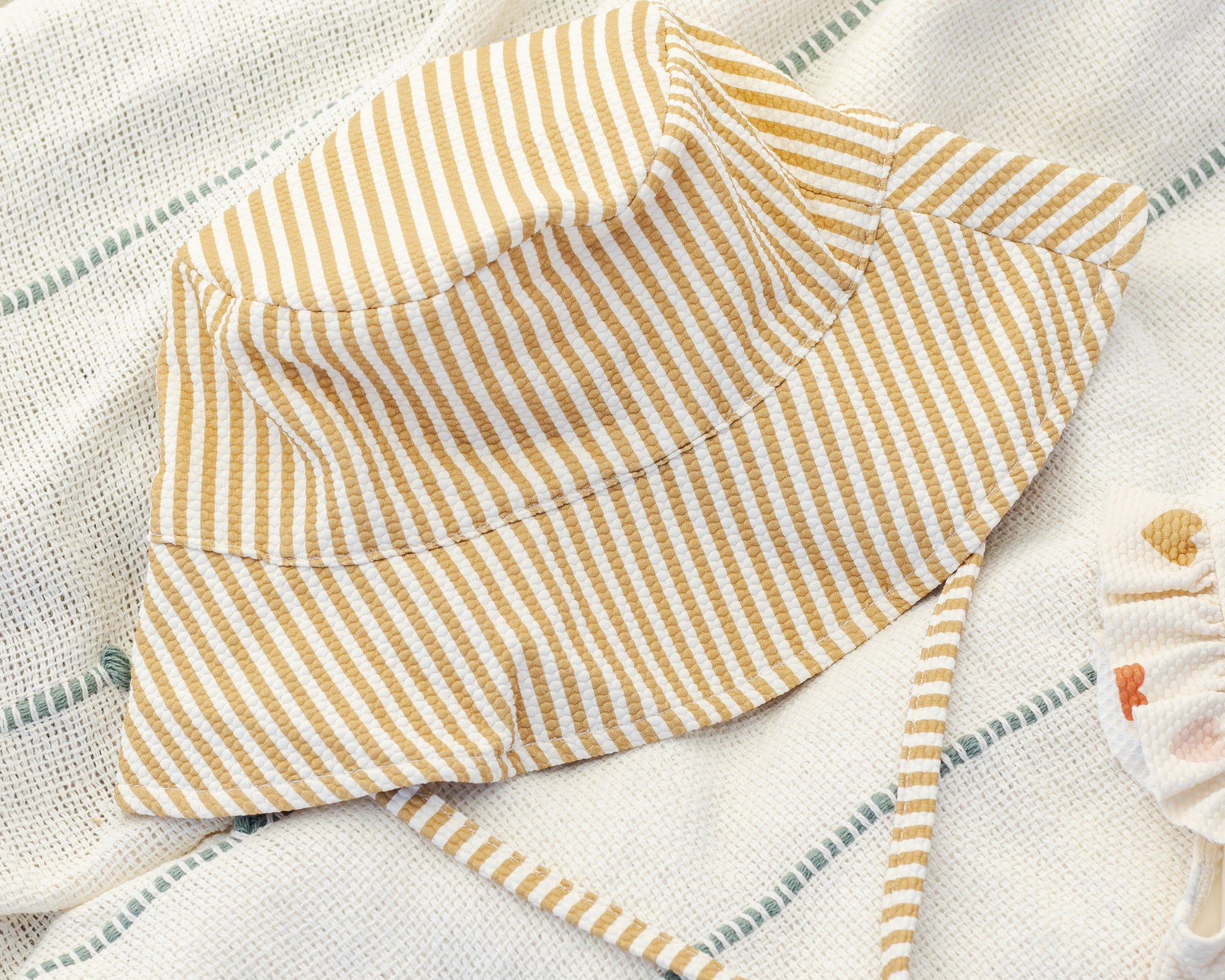 Rylee & Cru Youth Bucket Hat in Honey Stripe laid on a striped blanket