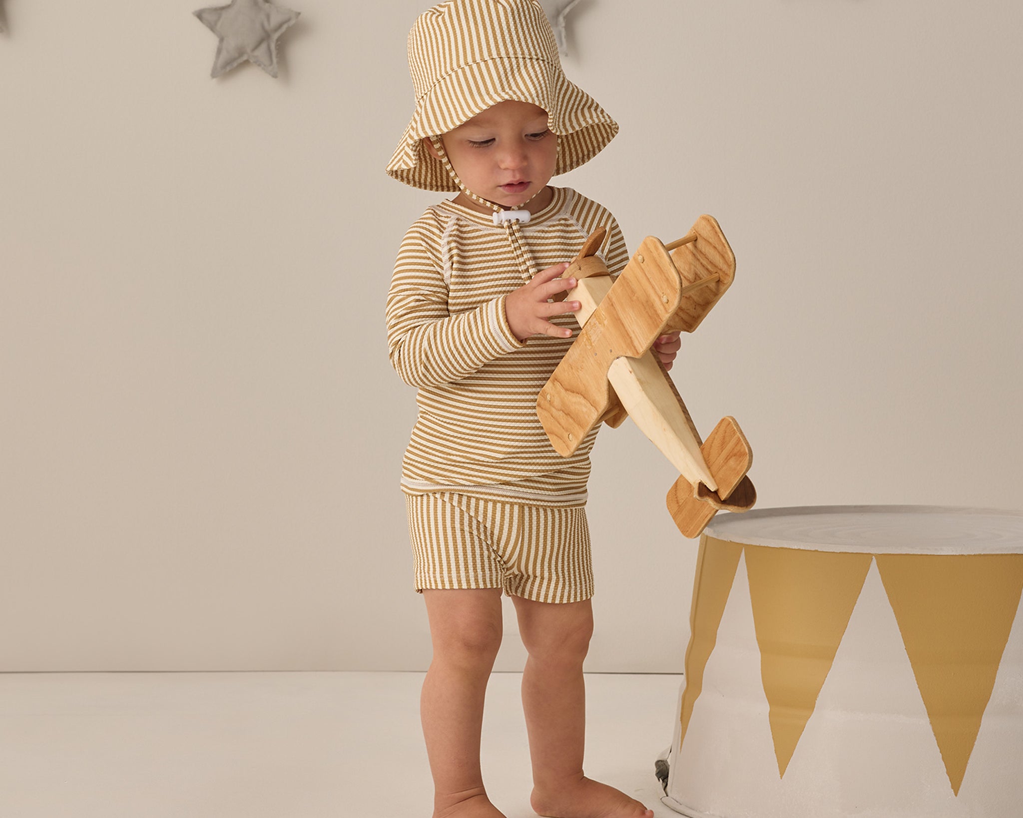 Toddler wearing the Rylee & Cru Youth Bucket Hat in Honey Stripe with a matching set, holding a wooden airplane