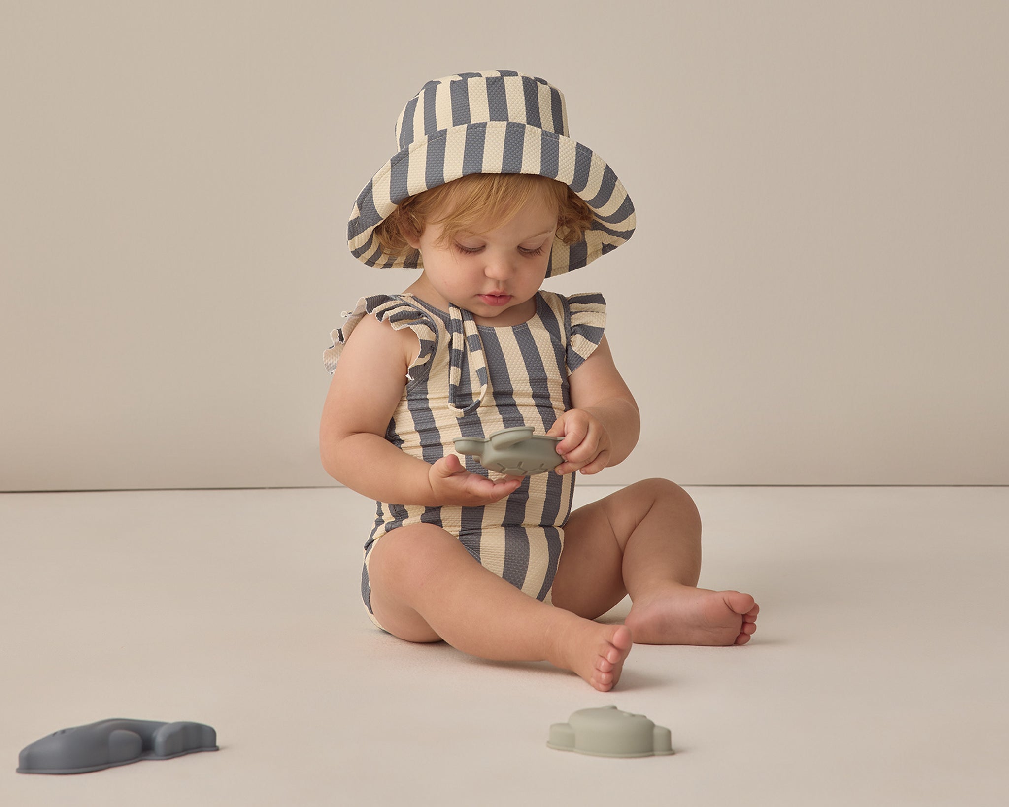 Baby playing with toys wearing the Rylee & Cru Youth Bucket Hat in Retro Stripe Ocean