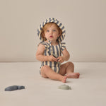 Baby sitting in a striped swimsuit wearing the Rylee & Cru Youth Bucket Hat in Retro Stripe Ocean