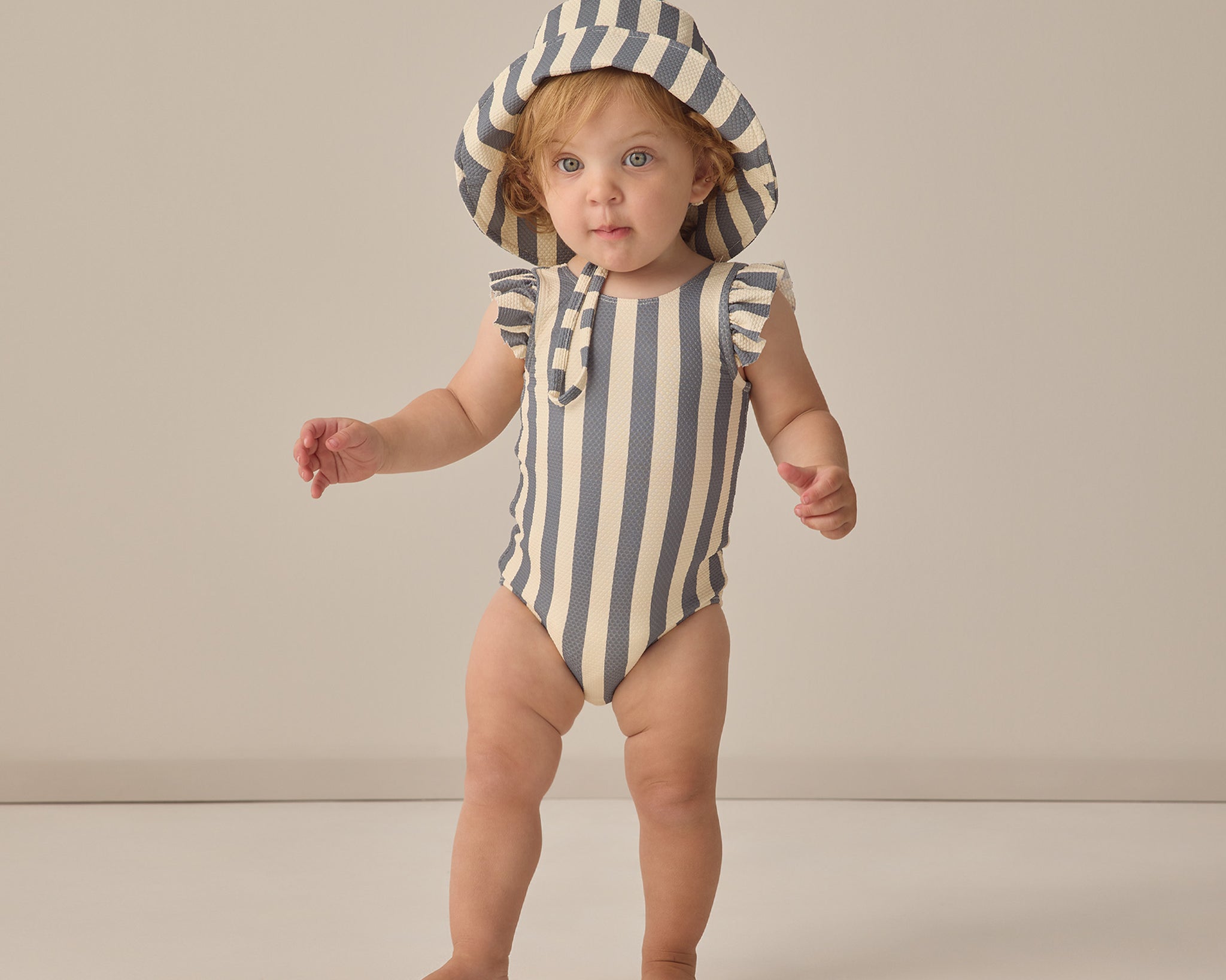 Toddler standing in a striped swimsuit wearing the Rylee & Cru Youth Bucket Hat in Retro Stripe Ocean