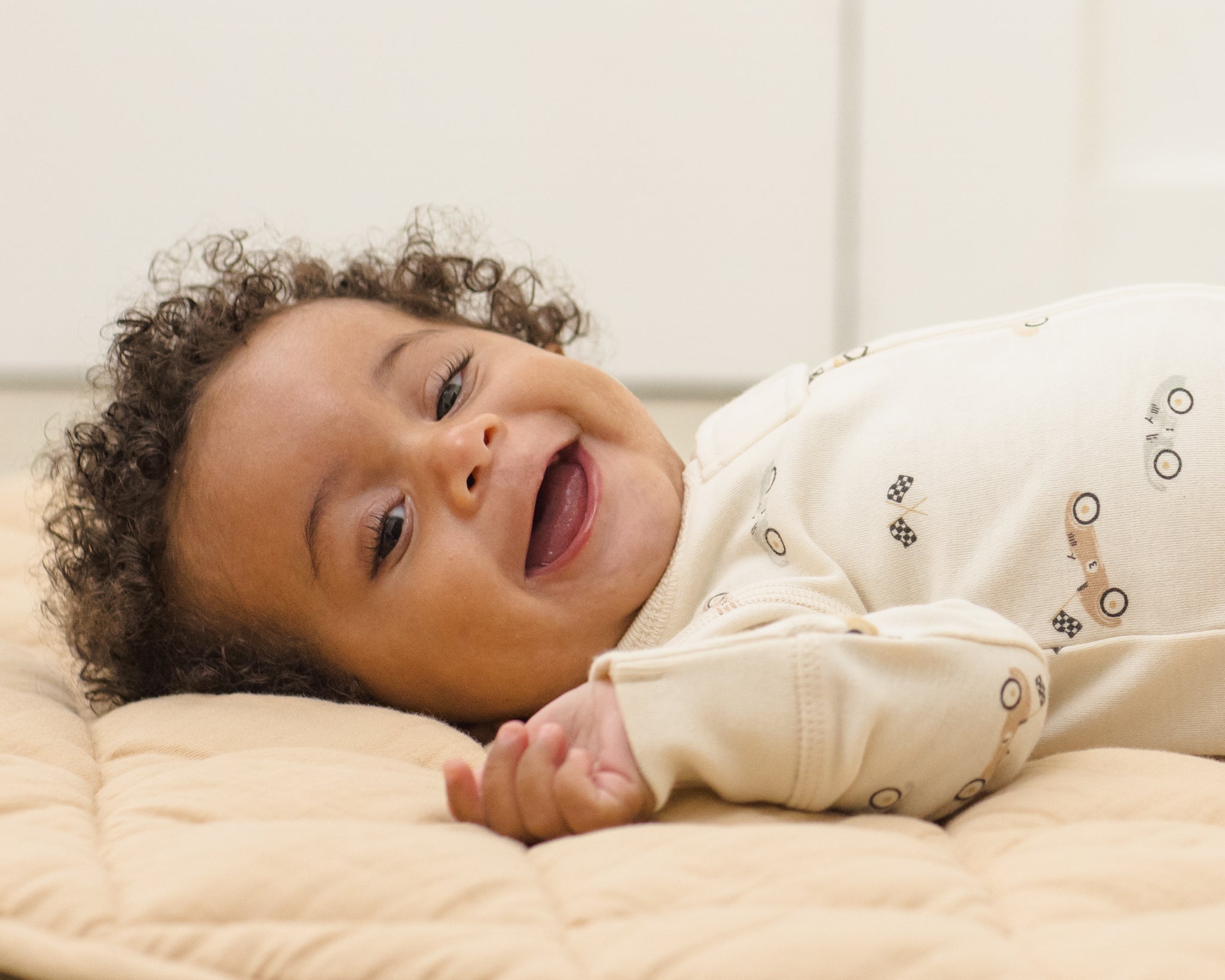 Laughing baby lying on a quilt wearing the Rylee & Cru Zip Longsleeve Sleeper in Race Car