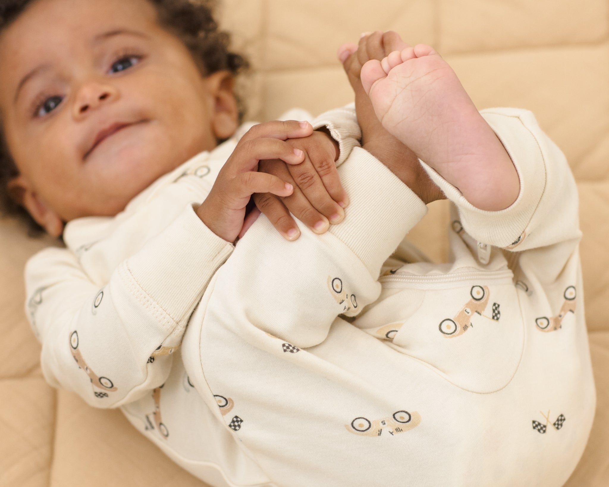 Baby lying on a quilt wearing the Rylee & Cru Zip Longsleeve Sleeper in Race Car, hands together