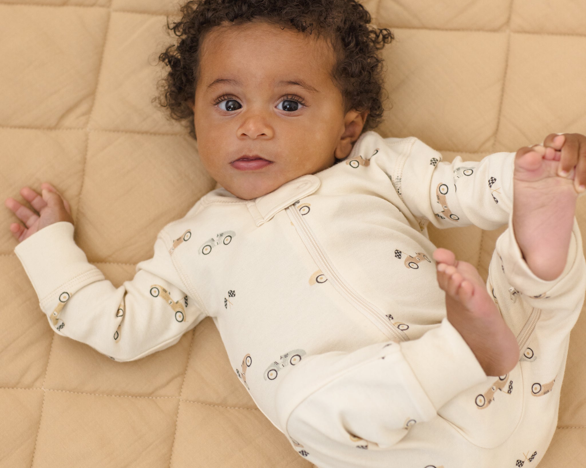 Baby stretched out on a quilt wearing the Rylee & Cru Zip Longsleeve Sleeper in Race Car