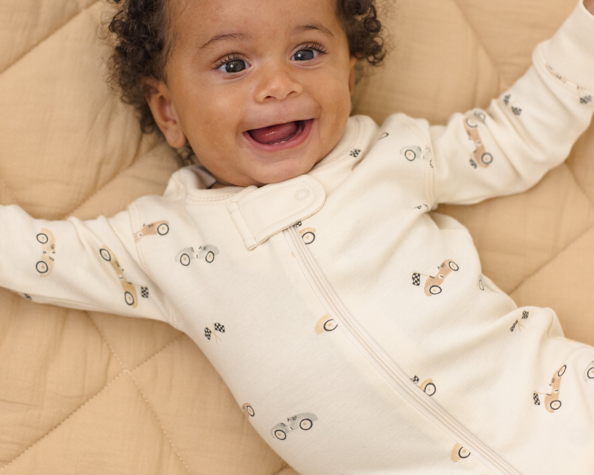 Smiling baby wearing the Rylee & Cru Zip Longsleeve Sleeper in Race Car, close-up