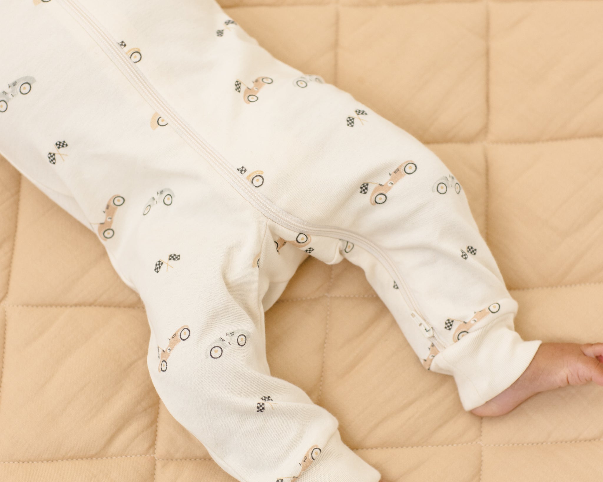 Rylee & Cru Zip Longsleeve Sleeper in Race Car laid flat on a quilt, showing the cream race car print