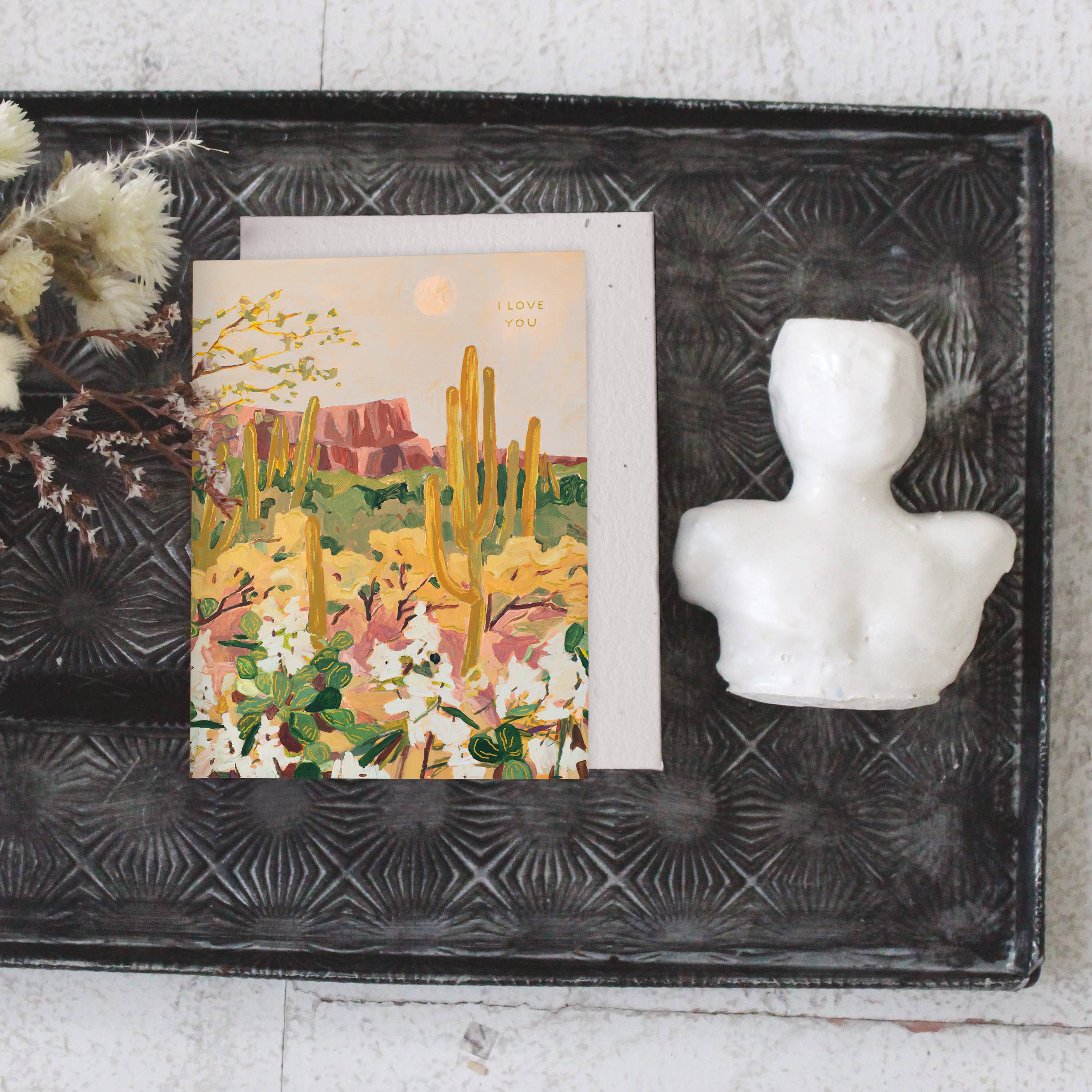Seedlings Desert Moonlight card on a black tray with dried flowers and a small white bust