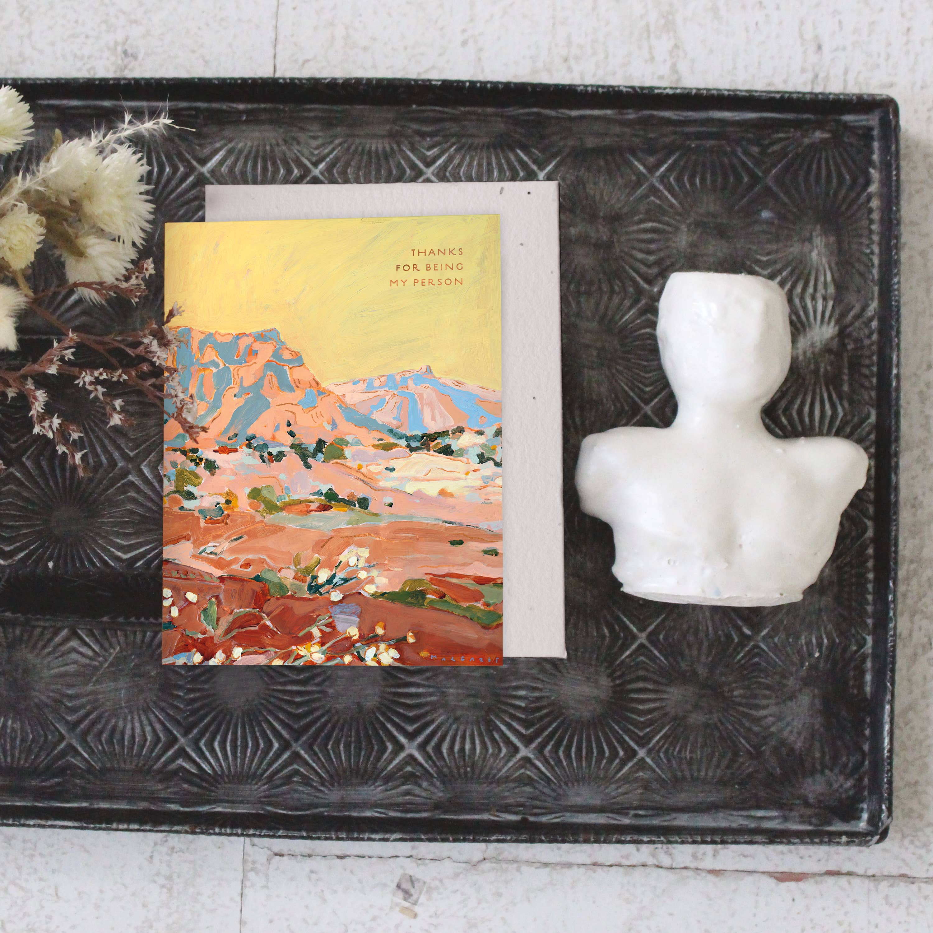 Seedlings Shadow Rocks card on a black tray with dried flowers and a small white bust