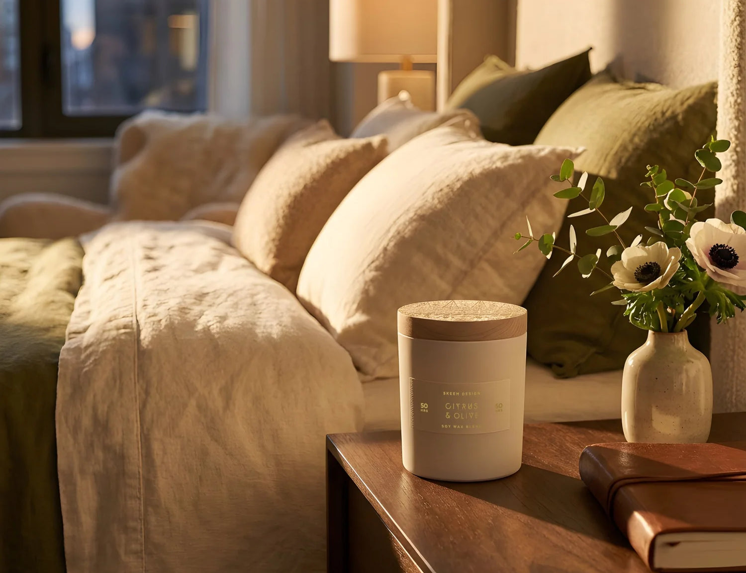 Skeem Black Currant Candle on a wooden nightstand beside a bed with white and olive bedding