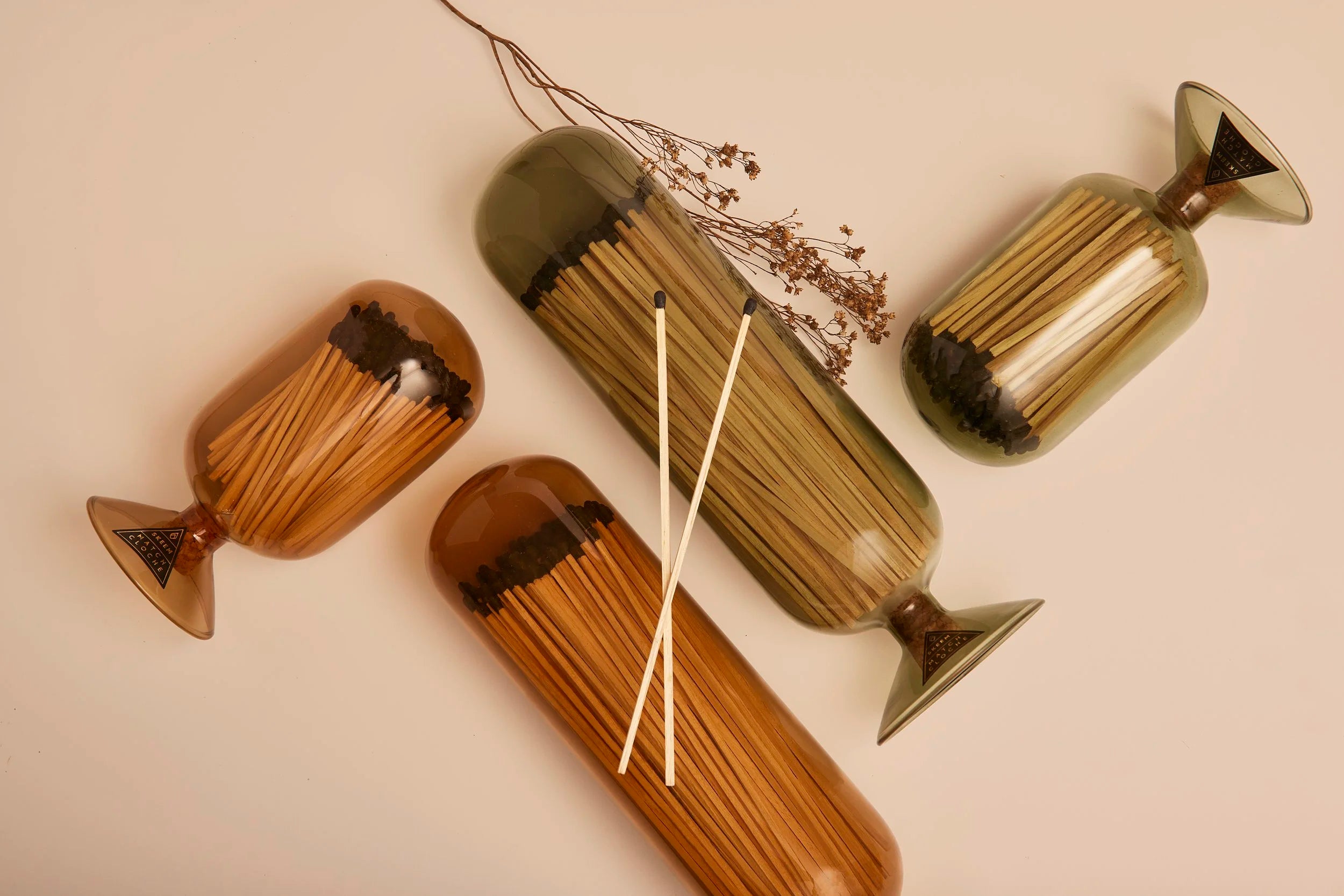 Skeem Match Cloches in amber and olive lying on their sides with dried botanicals