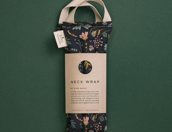 Slow North Hot + Cold Neck Wrap in Canyon Springs, a navy floral wrap with a kraft sleeve on a green background