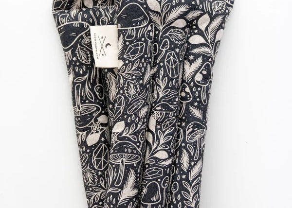 Slow North Hot + Cold Neck Wrap in Mystical Mushroom, a black wrap with cream mushroom line art, laid flat