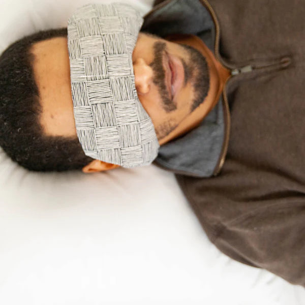 Man lying down wearing the Slow North Migraine Mask in Haystack over his eyes