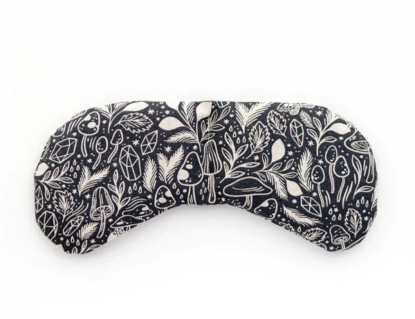 Slow North Migraine Mask in Mystical Mushroom, a black eye mask with cream mushroom line art, laid flat