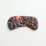 Slow North Migraine Mask in Pom Blossom, a navy eye mask with orange and blue florals, laid flat