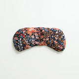 Slow North Migraine Mask in Pom Blossom, a navy eye mask with orange and blue florals, laid flat