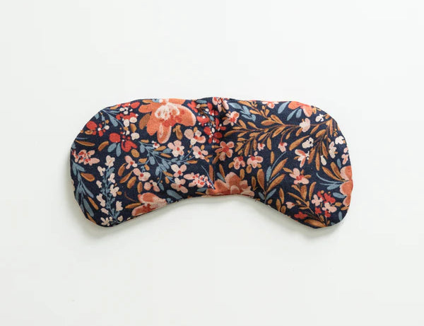 Slow North Migraine Mask in Pom Blossom, a navy eye mask with orange and blue florals, laid flat