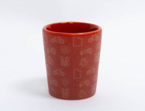 Soft red ceramic Moab shot glass with etched desert icons and a glossy interior