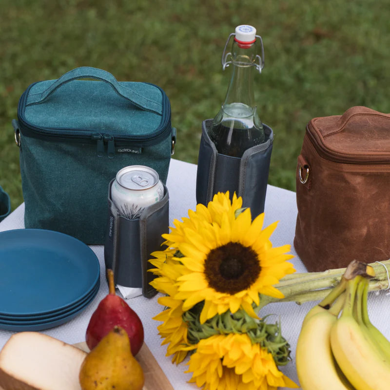 SoYoung Grey Wraparound Ice Pack wrapped around a glass bottle at a picnic with lunch bags and sunflowers