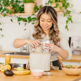Smiling woman packing the SoYoung Lunch Poche in cream pinstripe at a kitchen counter
