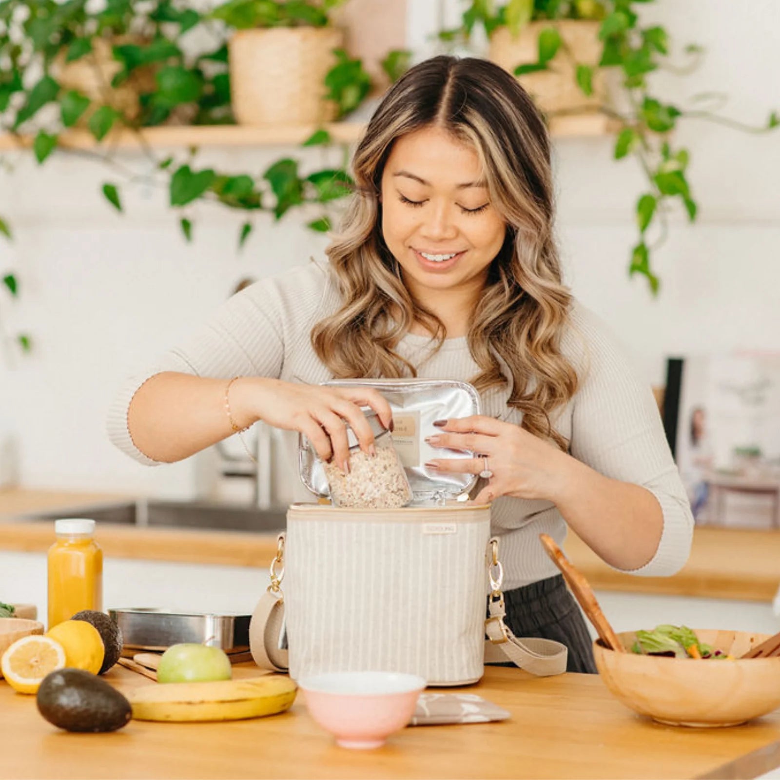 Smiling woman packing the SoYoung Lunch Poche in cream pinstripe at a kitchen counter