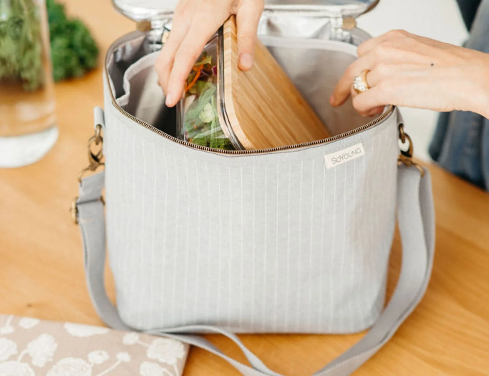 Hands packing food containers into the SoYoung Lunch Poche in gray at a kitchen table
