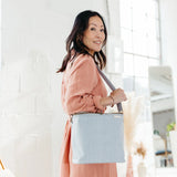 Smiling woman in a pink shirt carrying the SoYoung Lunch Poche in Pinstripe Heather Grey over her shoulder
