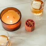 Tenn Prairie Concrete Match Holder in brick orange beside a lit amber candle and a glass of whiskey