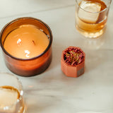 Tenn Prairie Concrete Match Holder in brick orange beside a lit amber candle and a glass of whiskey