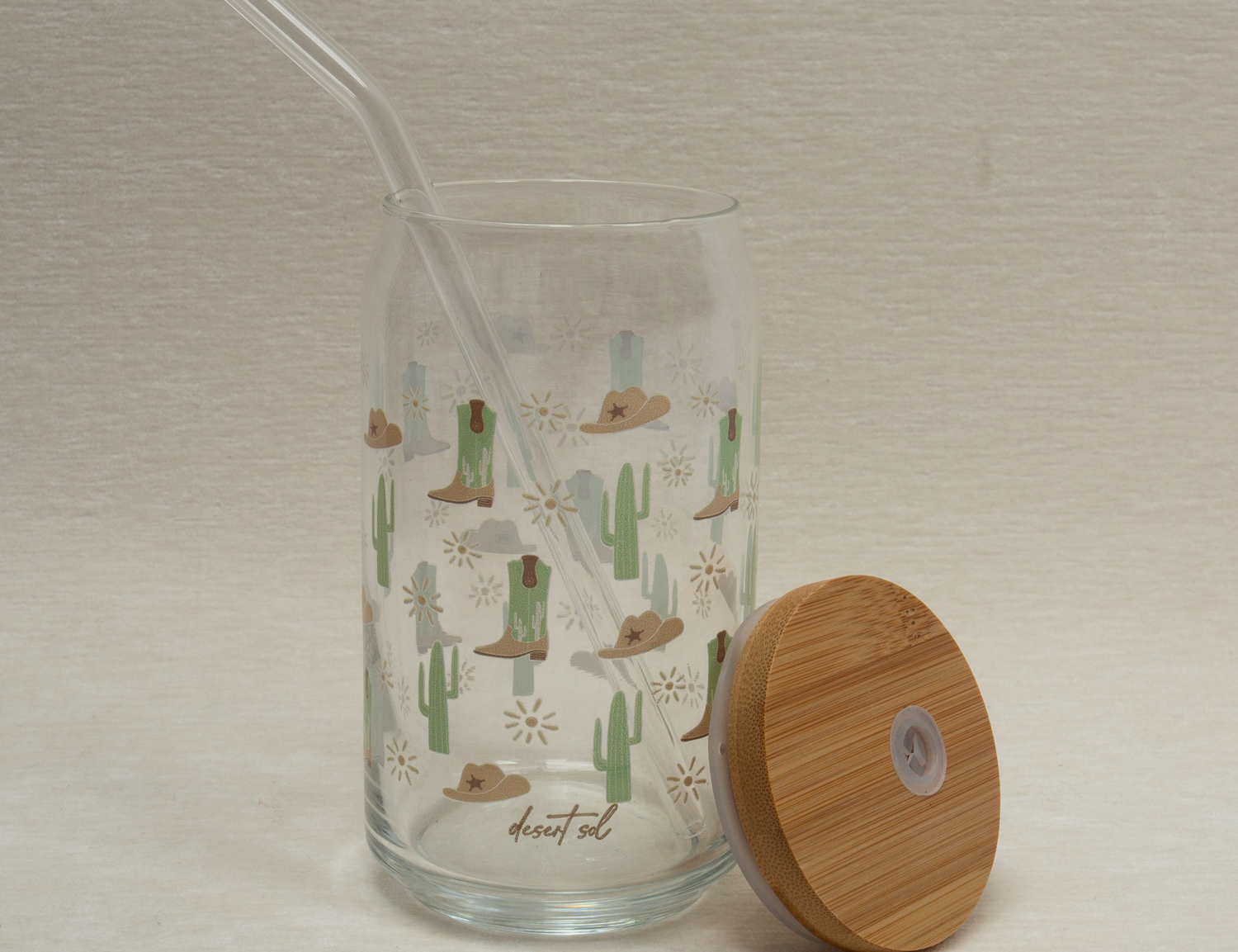The Care Co Cowboy Desert Glass Can with the bamboo lid resting beside it and a glass straw