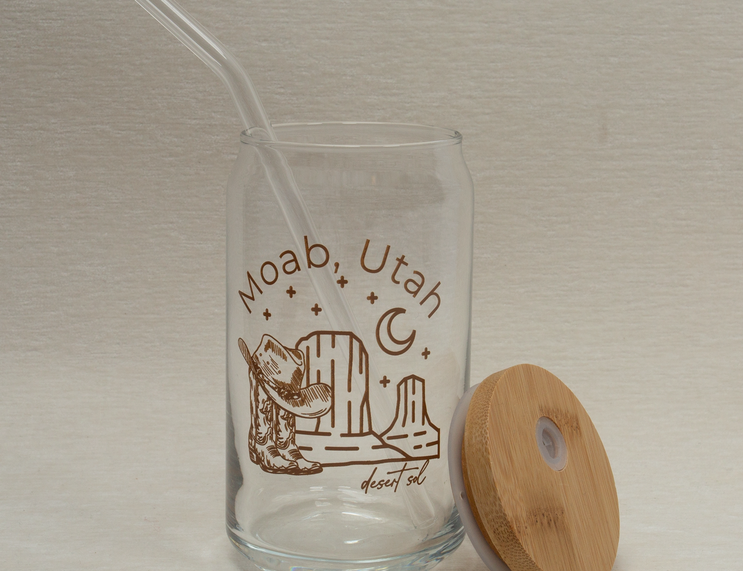 The Care Co Moab Desert Glass Can with the bamboo lid resting beside it and a glass straw