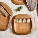 The Collective Belfort Crumb Brush Set on a linen table with wooden serving boards and fresh herbs