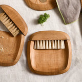 The Collective Belfort Crumb Brush Set on a linen table with wooden serving boards and fresh herbs