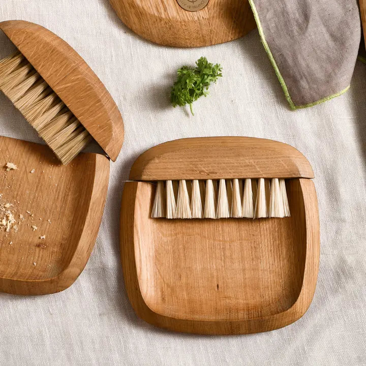 The Collective Belfort Crumb Brush Set on a linen table with wooden serving boards and fresh herbs