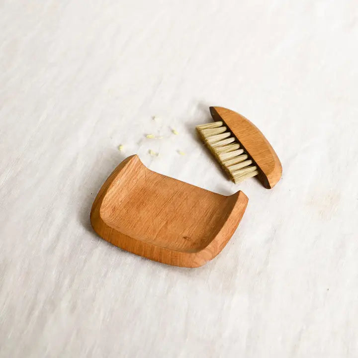 The Collective Belfort Crumb Brush Set, a natural wood dustpan and bristle brush on white linen