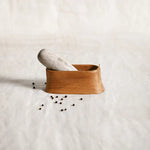 The Collective Belfort Oak Mortar and Marble Pestle with scattered peppercorns on white linen