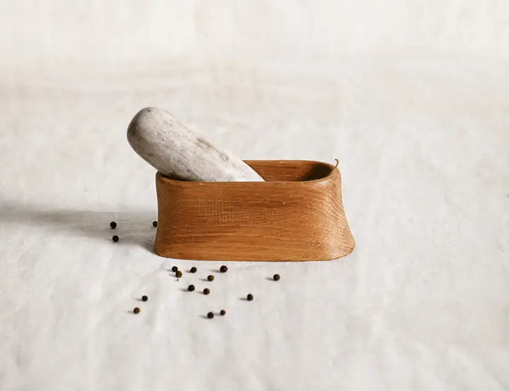 The Collective Belfort Oak Mortar and Marble Pestle with scattered peppercorns on white linen