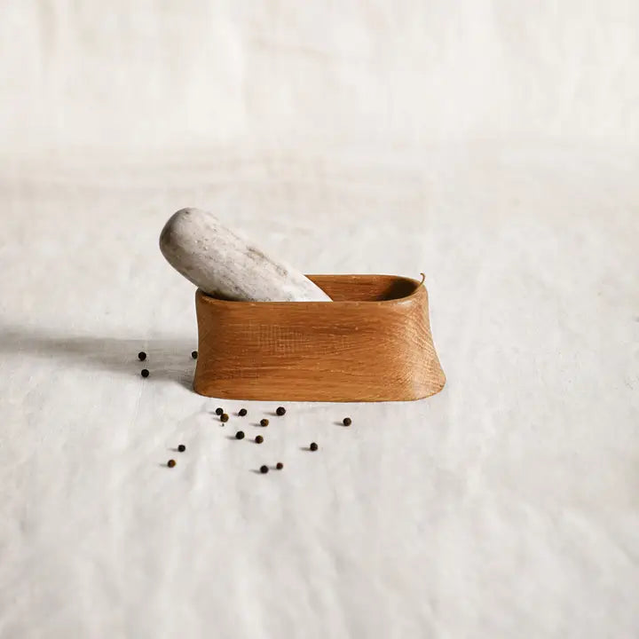 The Collective Belfort Oak Mortar and Marble Pestle with scattered peppercorns on white linen