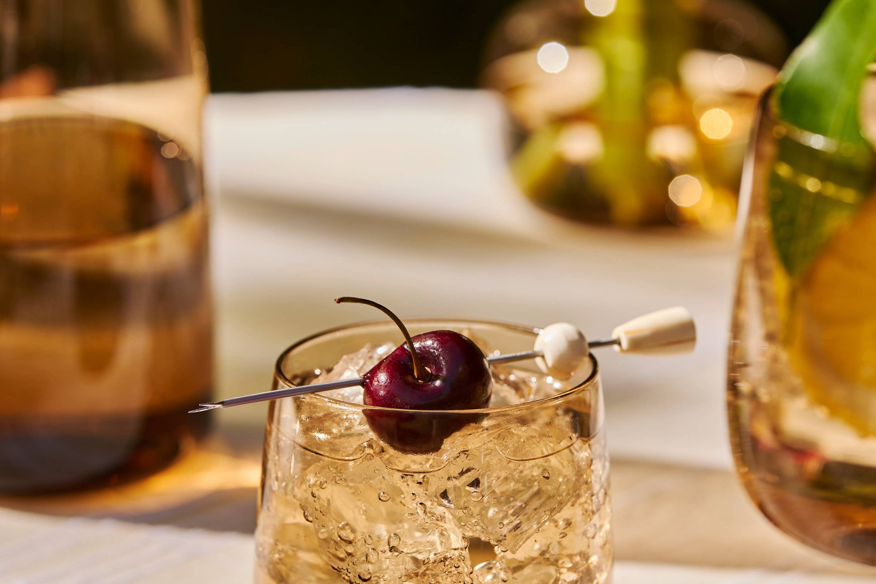 The Collective Ember Tumblers Set of 4, amber glass tumblers with cocktails and cherries on a table
