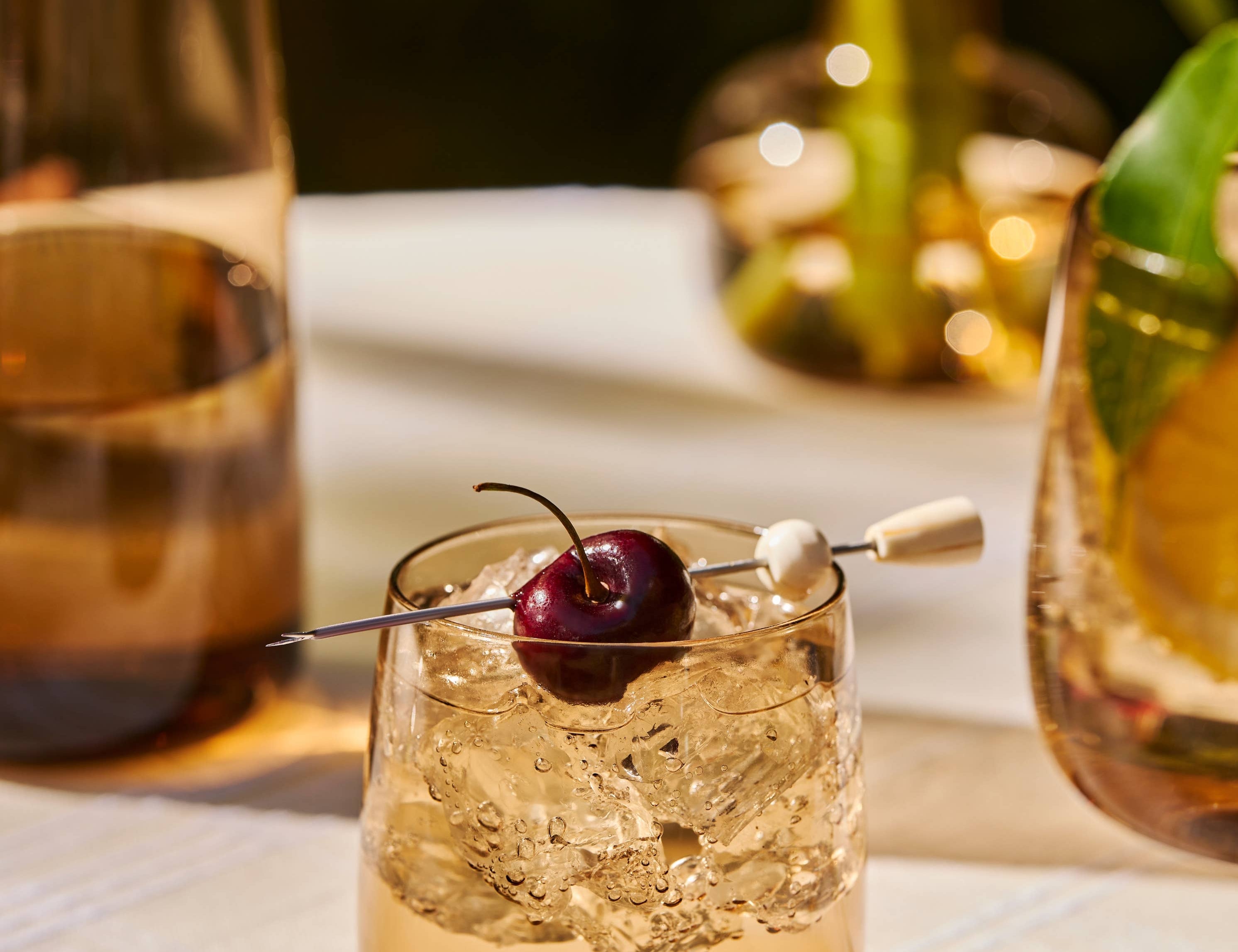 The Collective Ember Tumblers Set of 4, amber glass tumblers with cocktails and cherries on a table