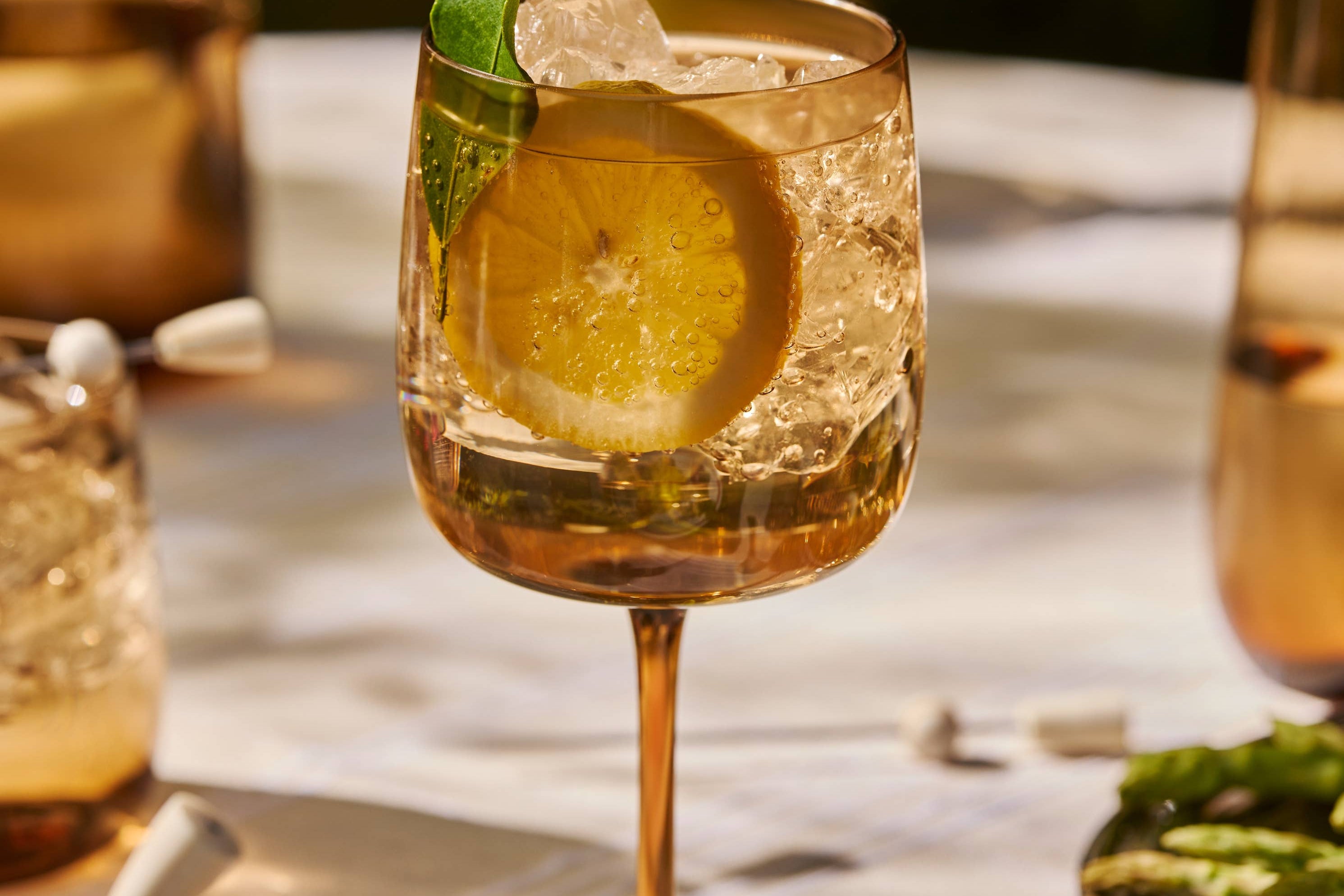 The Collective Ember Wine Glass with a spritz, lemon and herb garnish on an outdoor table