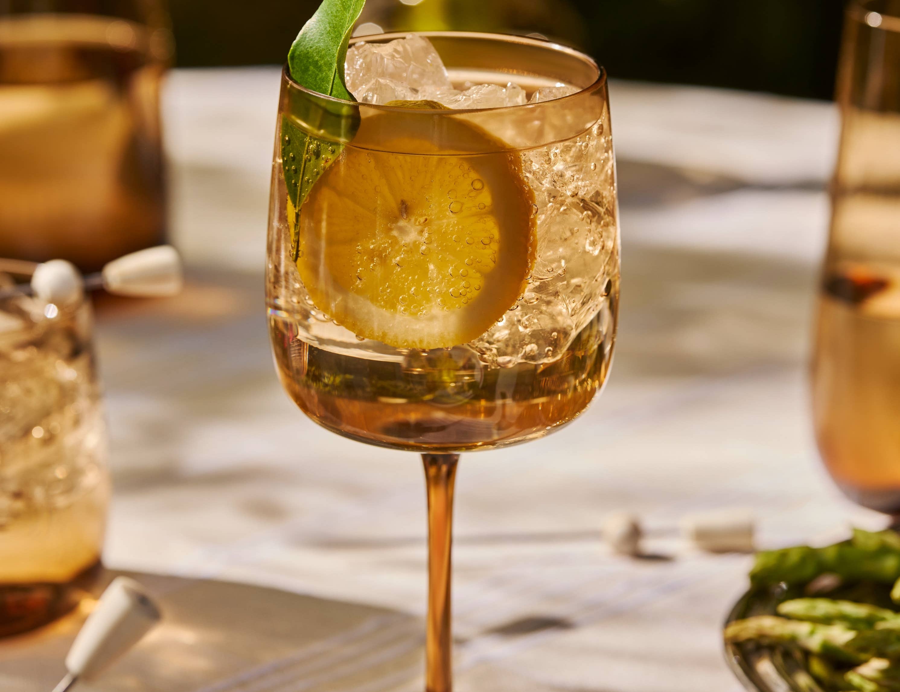 The Collective Ember Wine Glass with a spritz, lemon and herb garnish on an outdoor table