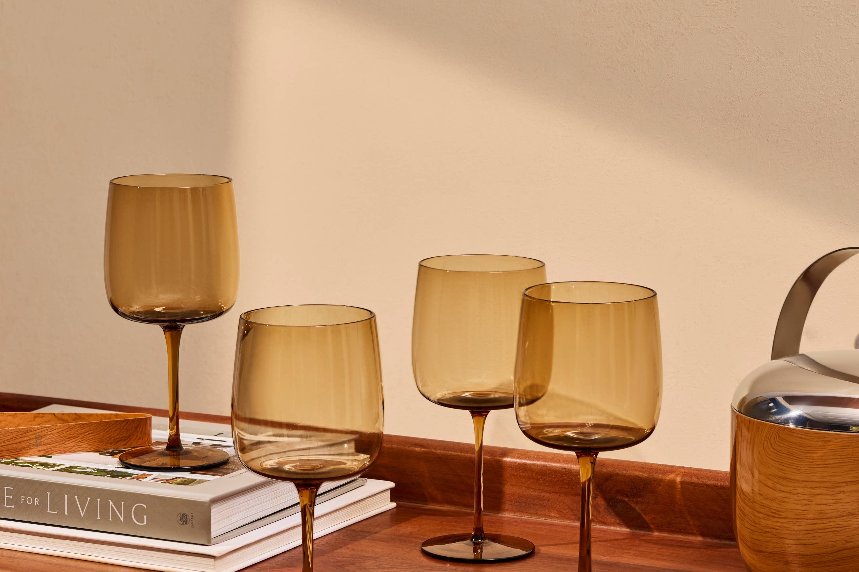 The Collective Ember Wine Glasses Set of 4 in amber glass on a wooden table beside books